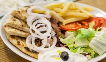 Il pitagyros al piatto: carne di maiale arrostita farcita con pomodoro, cipolla, patate fritte, insalata, salsa tzatziki, pita